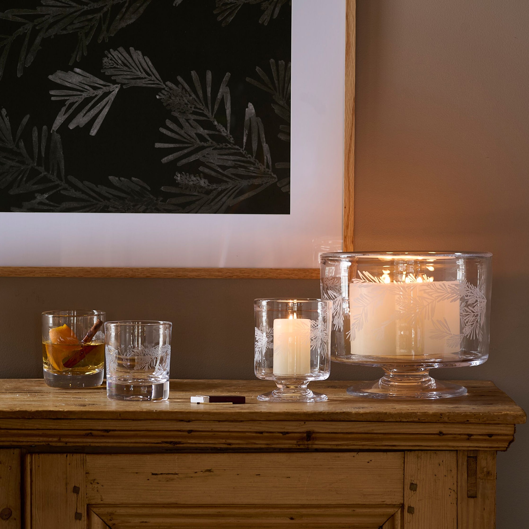 Two clear double old-fashioned glasses with engraved pine needle design, one containing amber liquid and one empty.