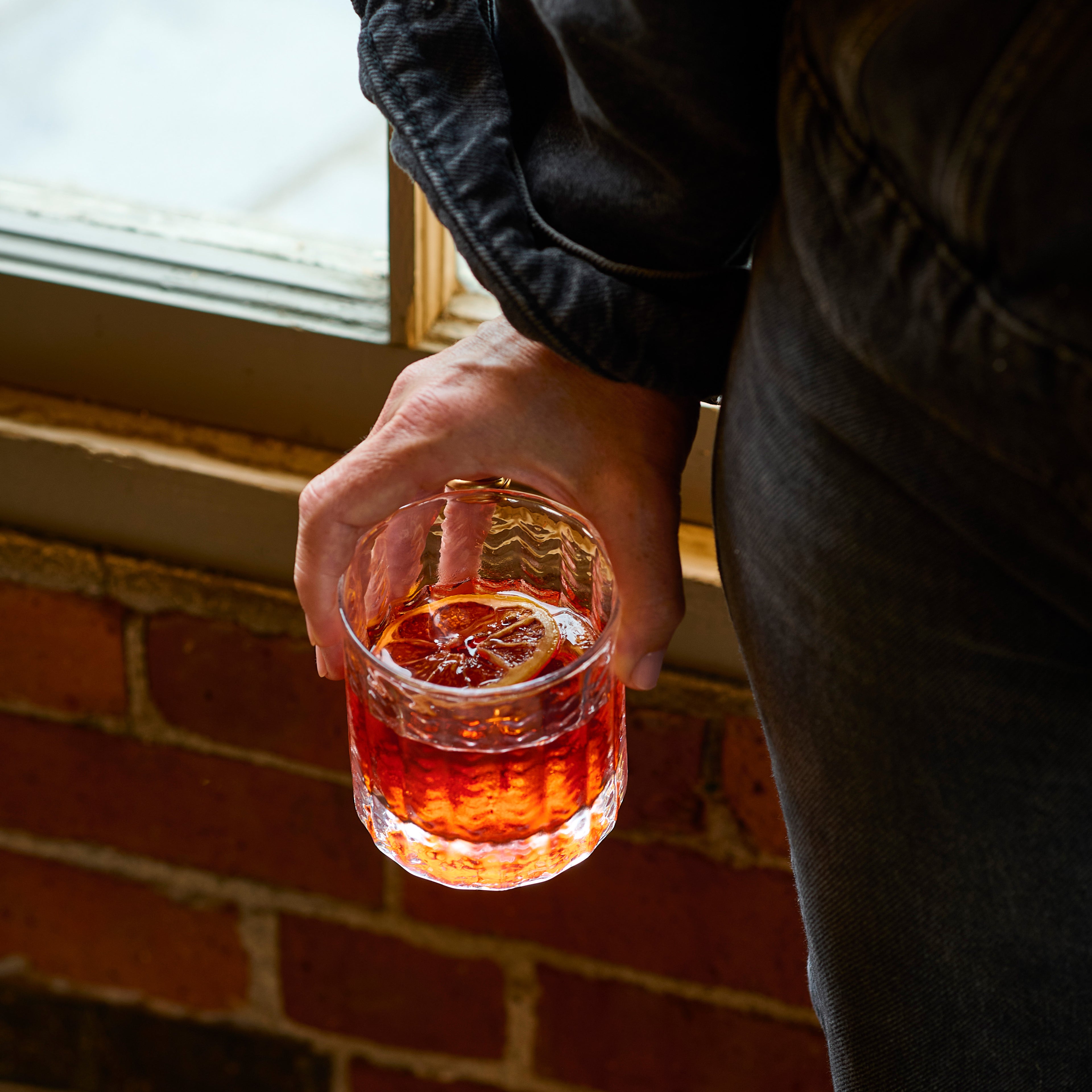 Hand holding a clear lowball glass filled with amber liquid and ice.