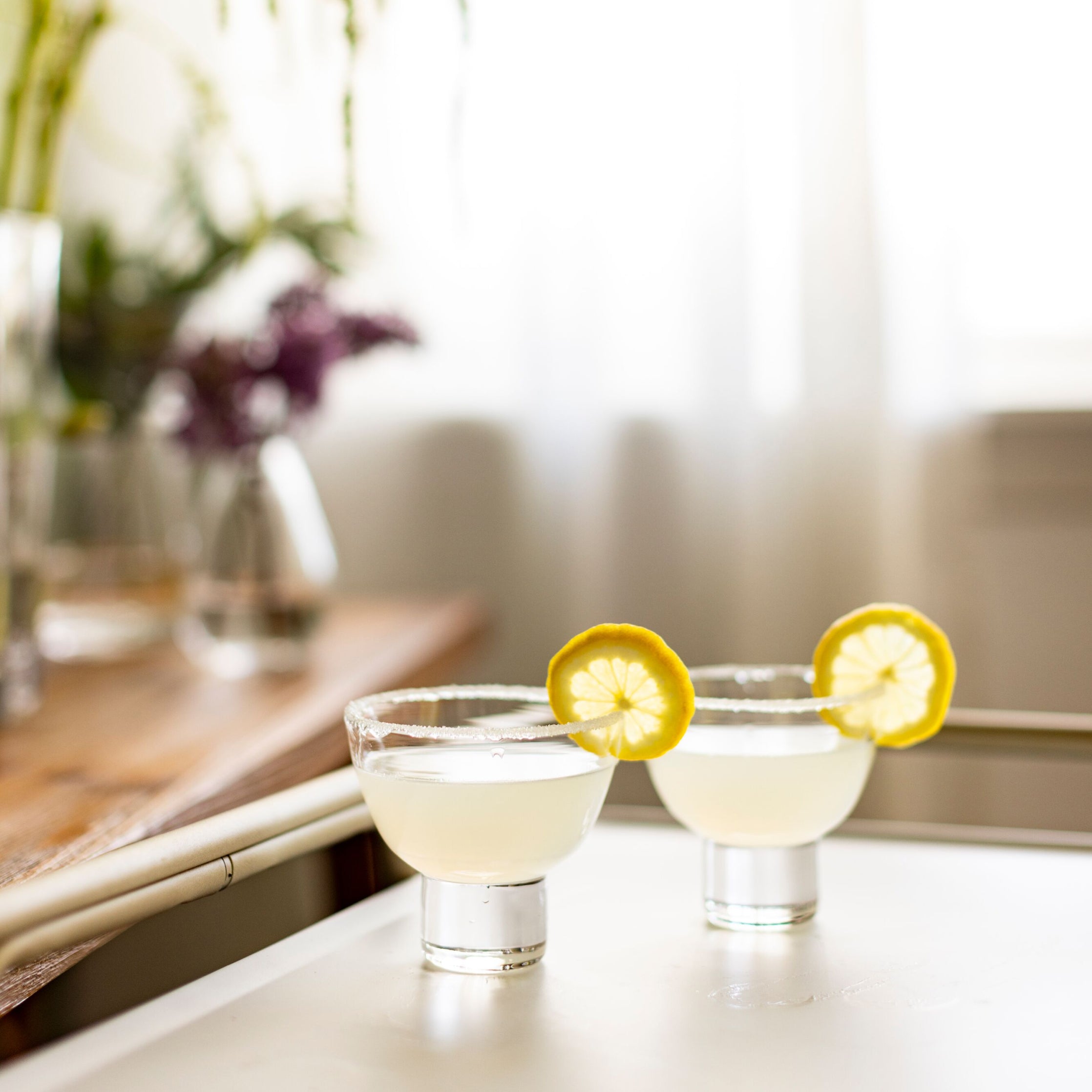 Two martini glasses filled with clear liquid and garnished with lemon slices on a white surface.