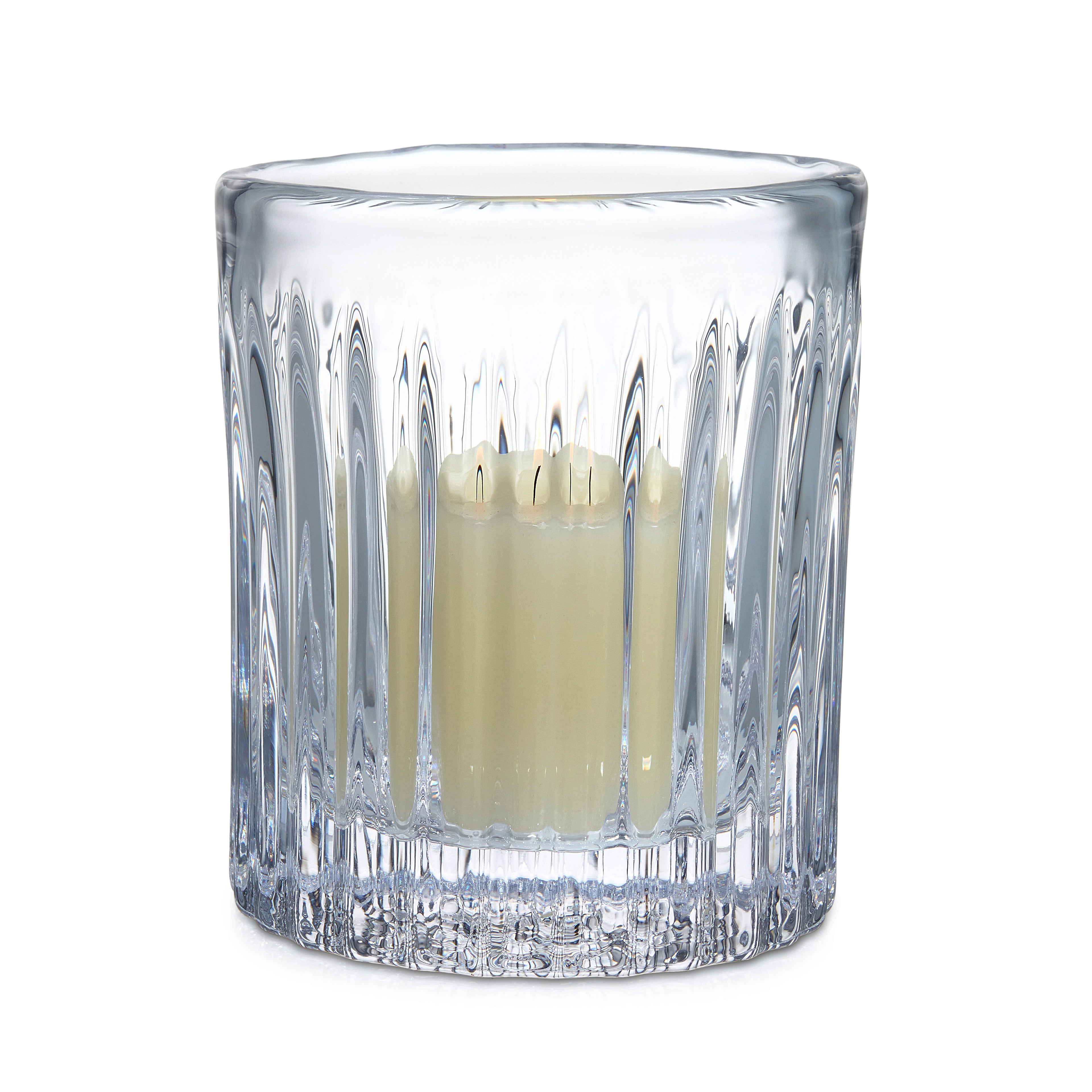 Clear crystal hurricane vase with vertical ribbed pattern holding lit cream-colored candle.