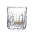 Clear glass tealight holder with vertical ribbed pattern containing lit cream-colored candle.
