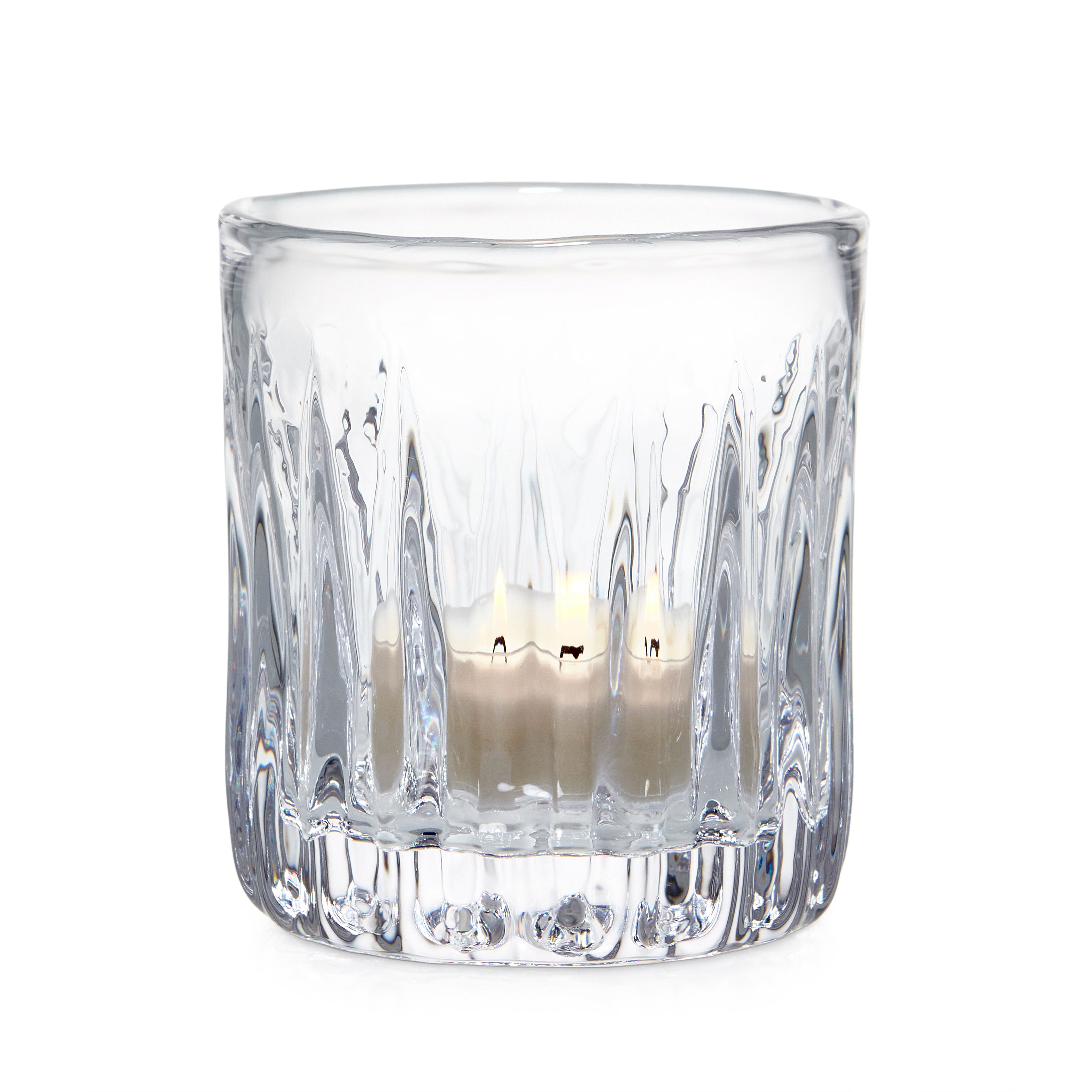 Clear glass tealight holder with vertical ribbed pattern containing lit cream-colored candle.