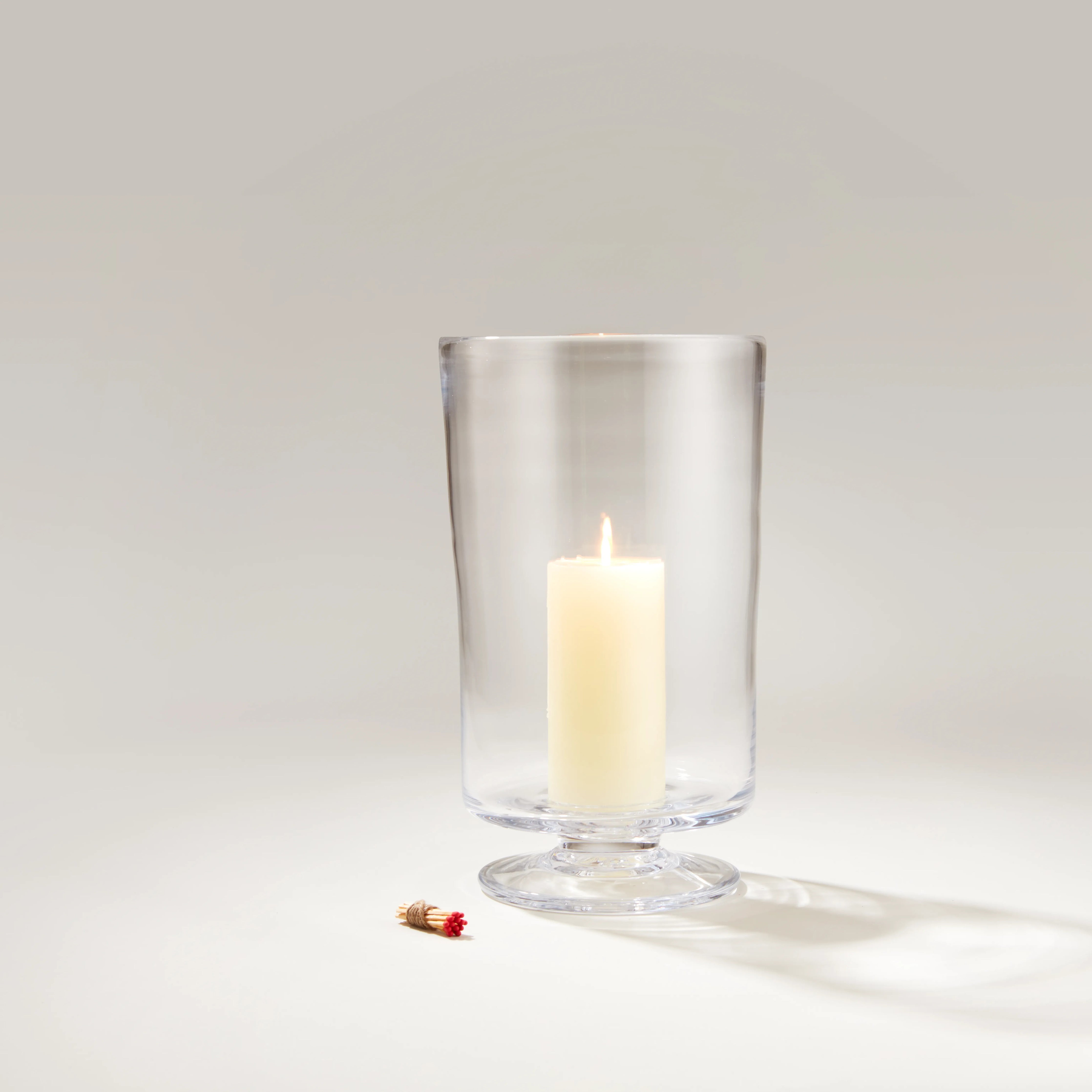 Candles in glass holders on a wooden table in a lush garden setting.