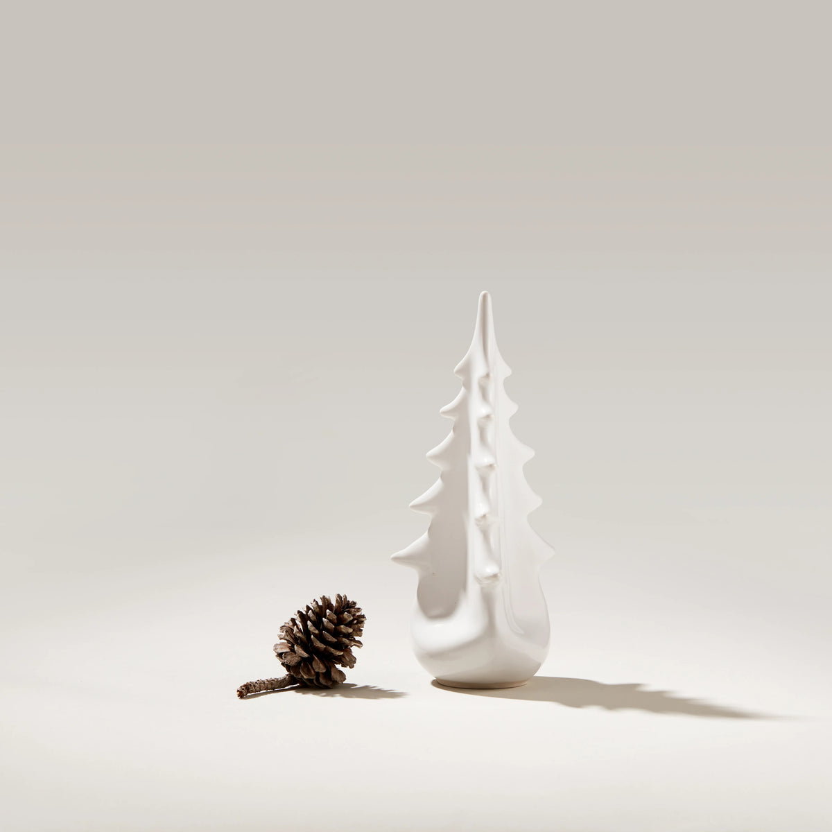 White ceramic evergreen tree-shaped vessel with pointed branches, displayed next to a pinecone.