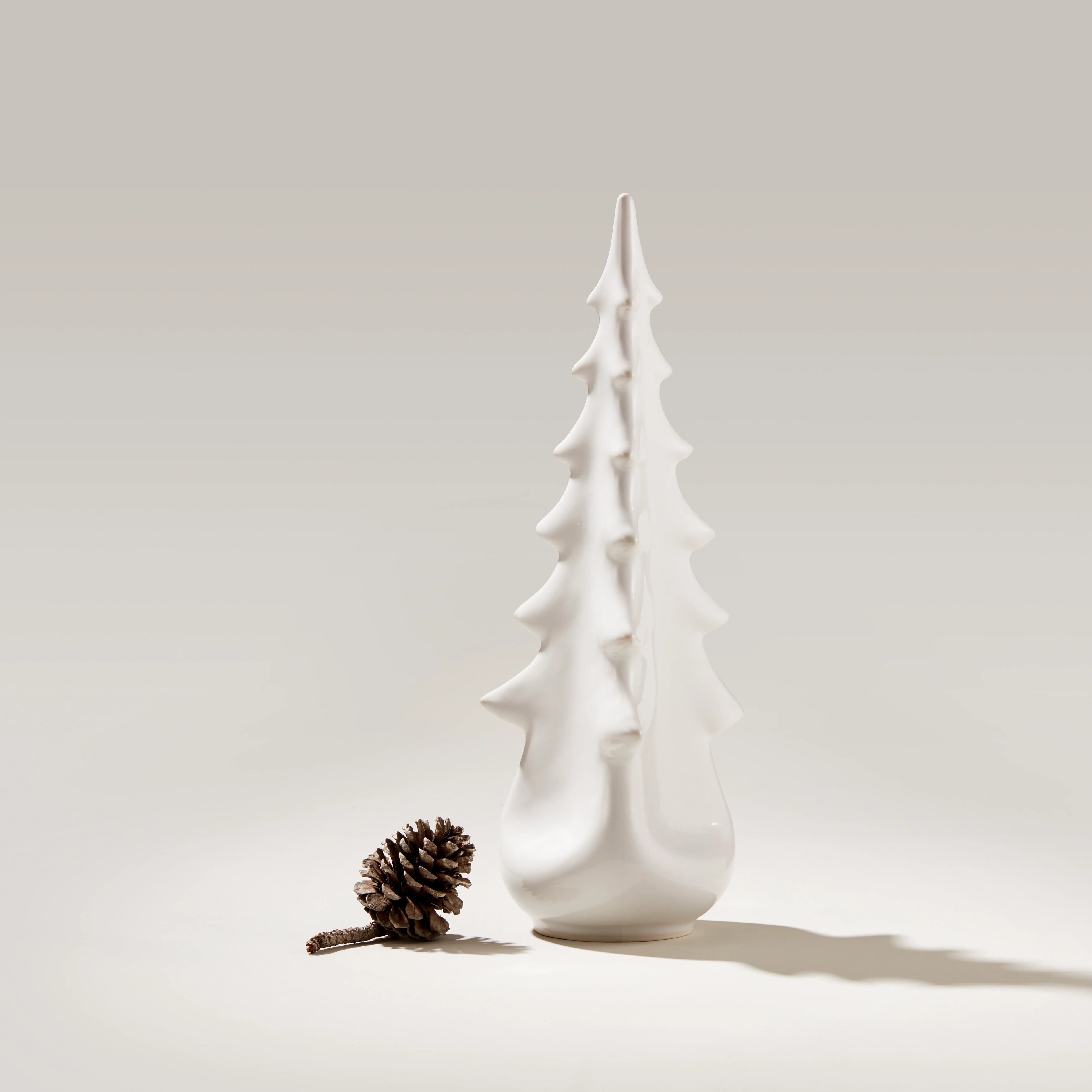 White ceramic tree-shaped vessel with tiered branches and rounded base, displayed next to a pinecone.