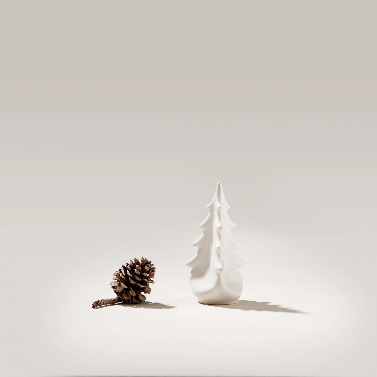 White ceramic evergreen tree-shaped vase with pointed top and tiered silhouette next to a pinecone.