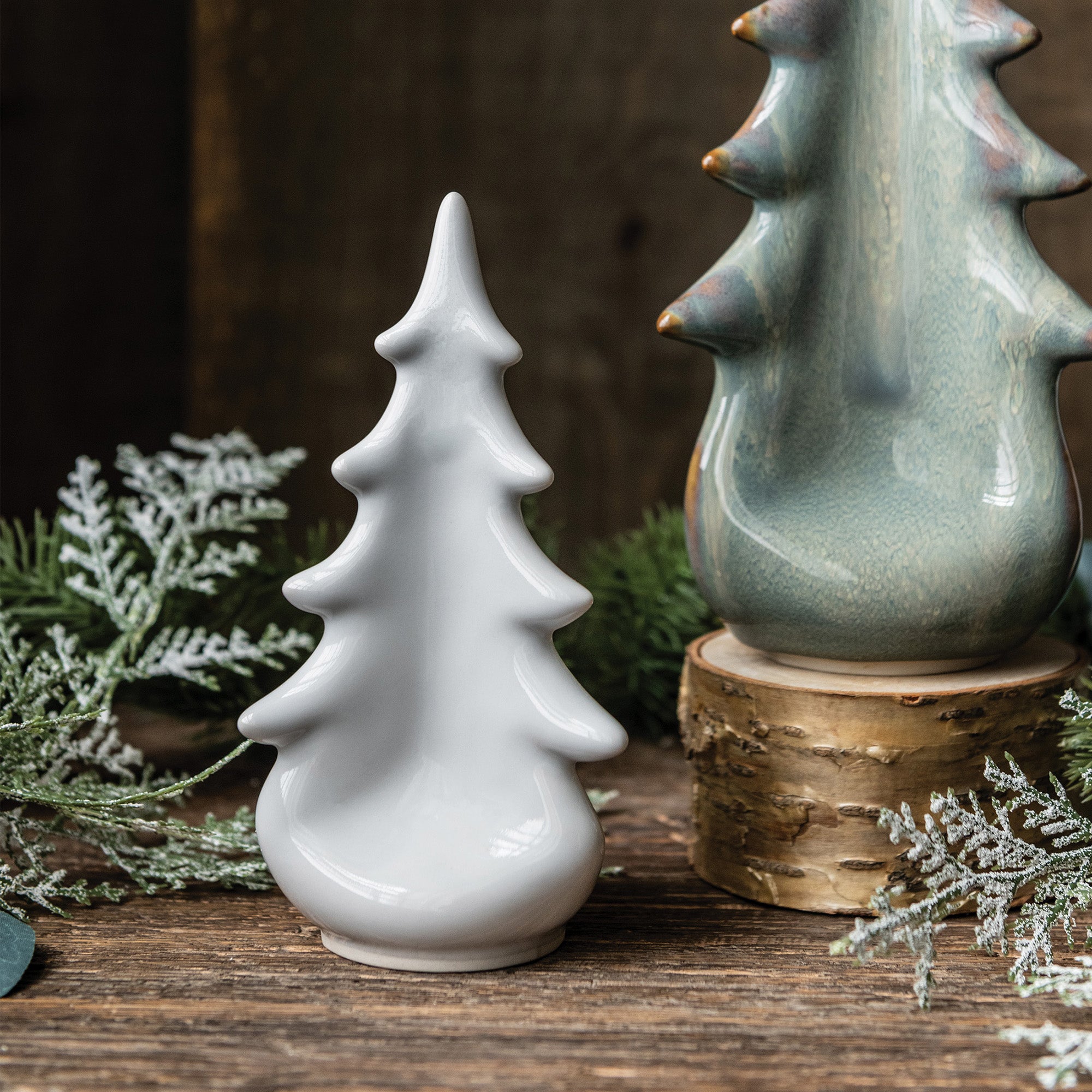 White ceramic tree-shaped decoration with pointed branches and rounded base, displayed with green ceramic vessel and greenery