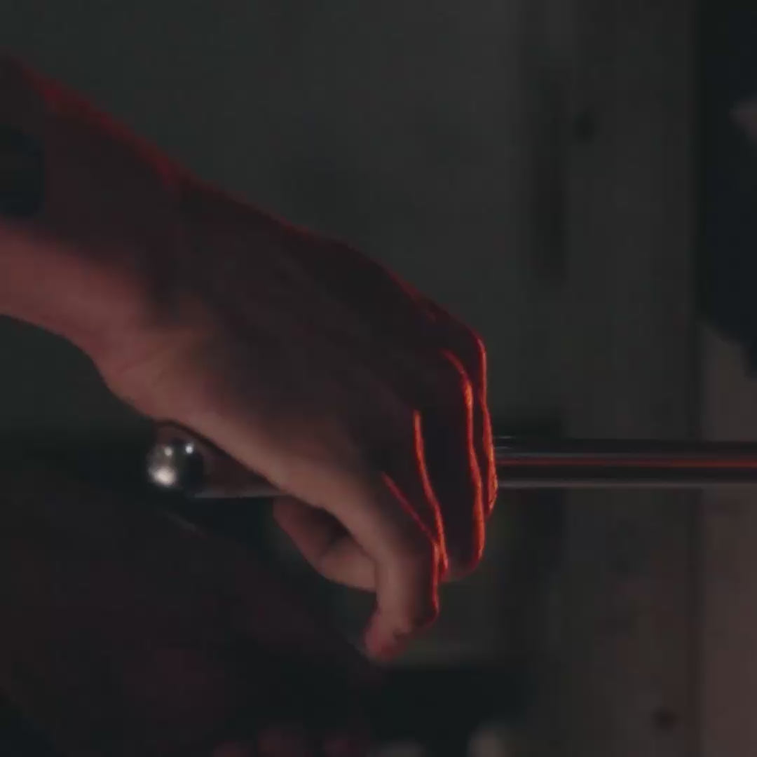 Video of a rod being turned by hands inside of a furnace used to melt glass