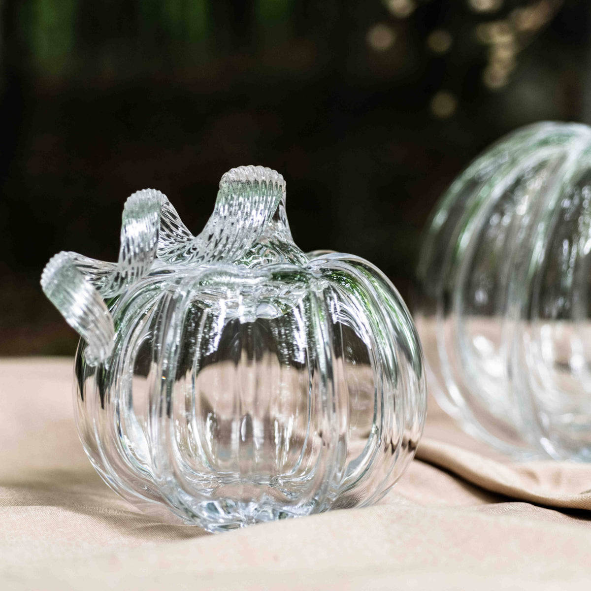 Three clear glass pumpkin-shaped containers with ridged details and stem tops on a beige surface.
