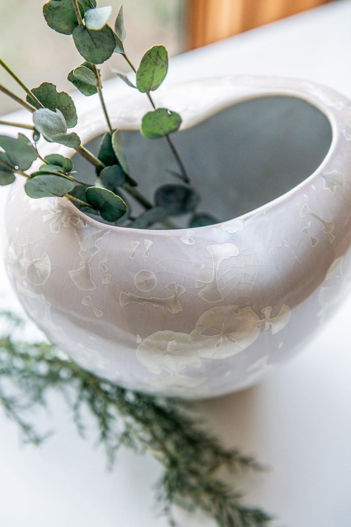 White ceramic vase with translucent floral pattern containing green eucalyptus stems and small white flowers.