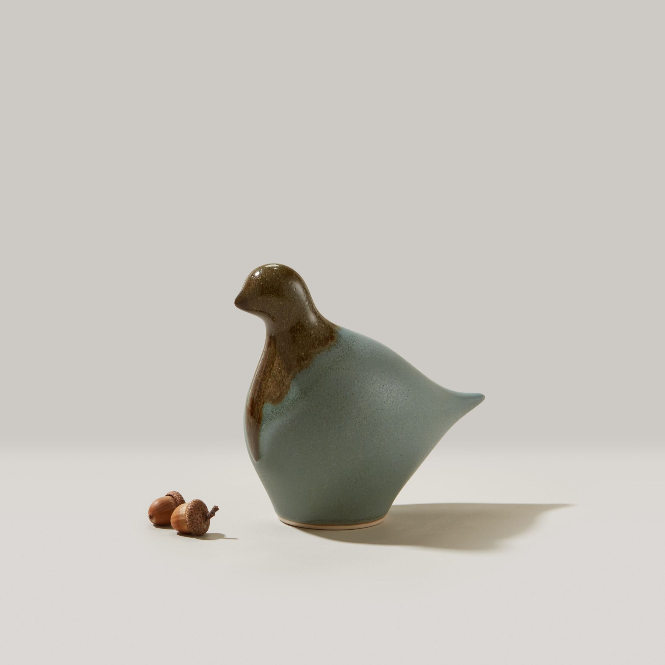 Ceramic dove figurine with brown head and sage green body, displayed with small acorns.