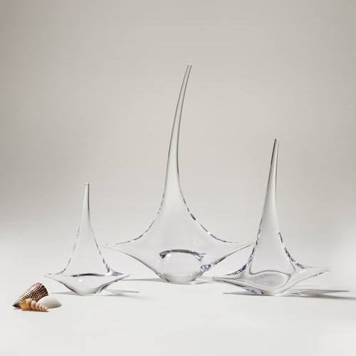 Three glass sailboat figurines with blue accents, displayed with small shells on white surface.
