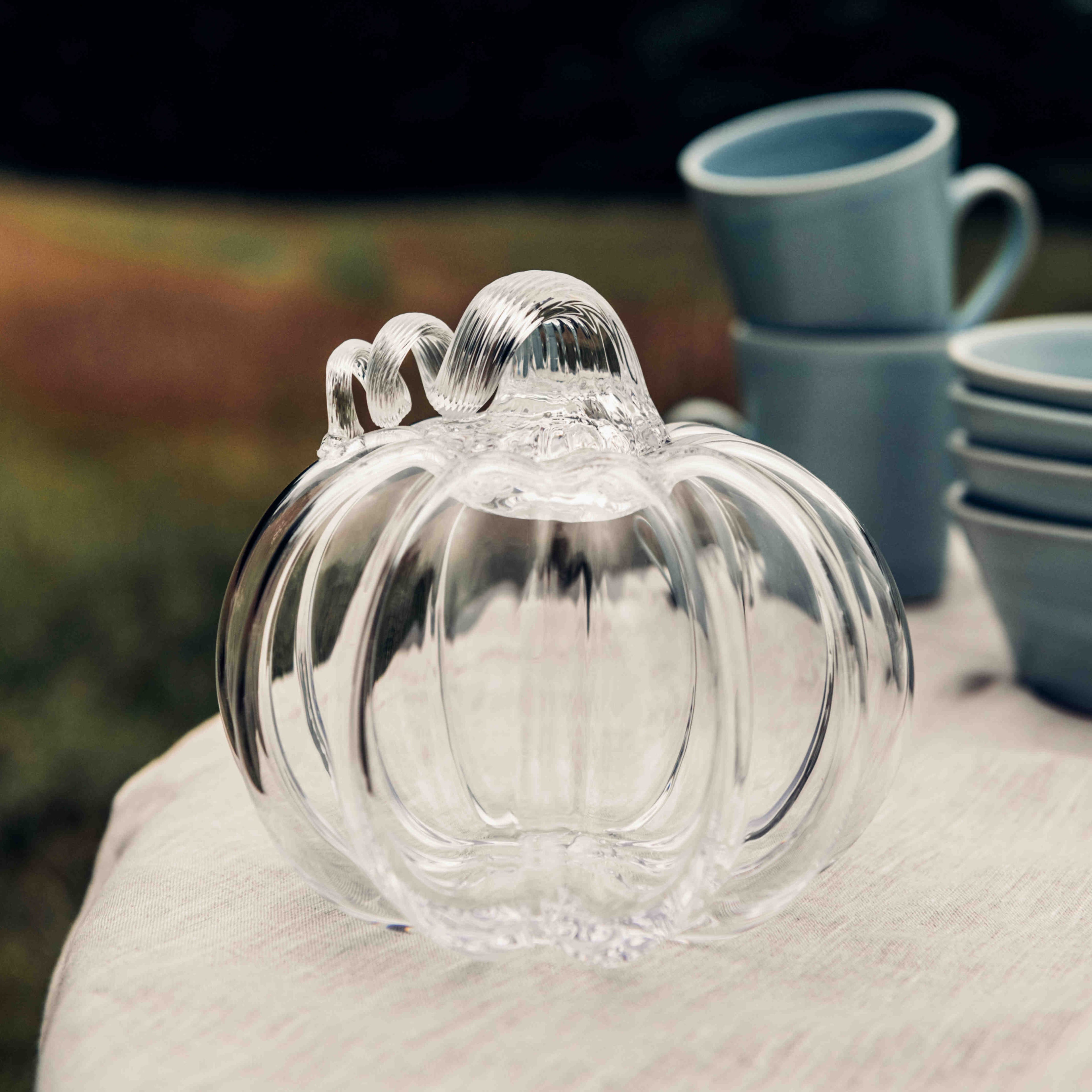 Clear glass pumpkin-shaped decorative piece with ribbed texture and stem on white fabric surface.