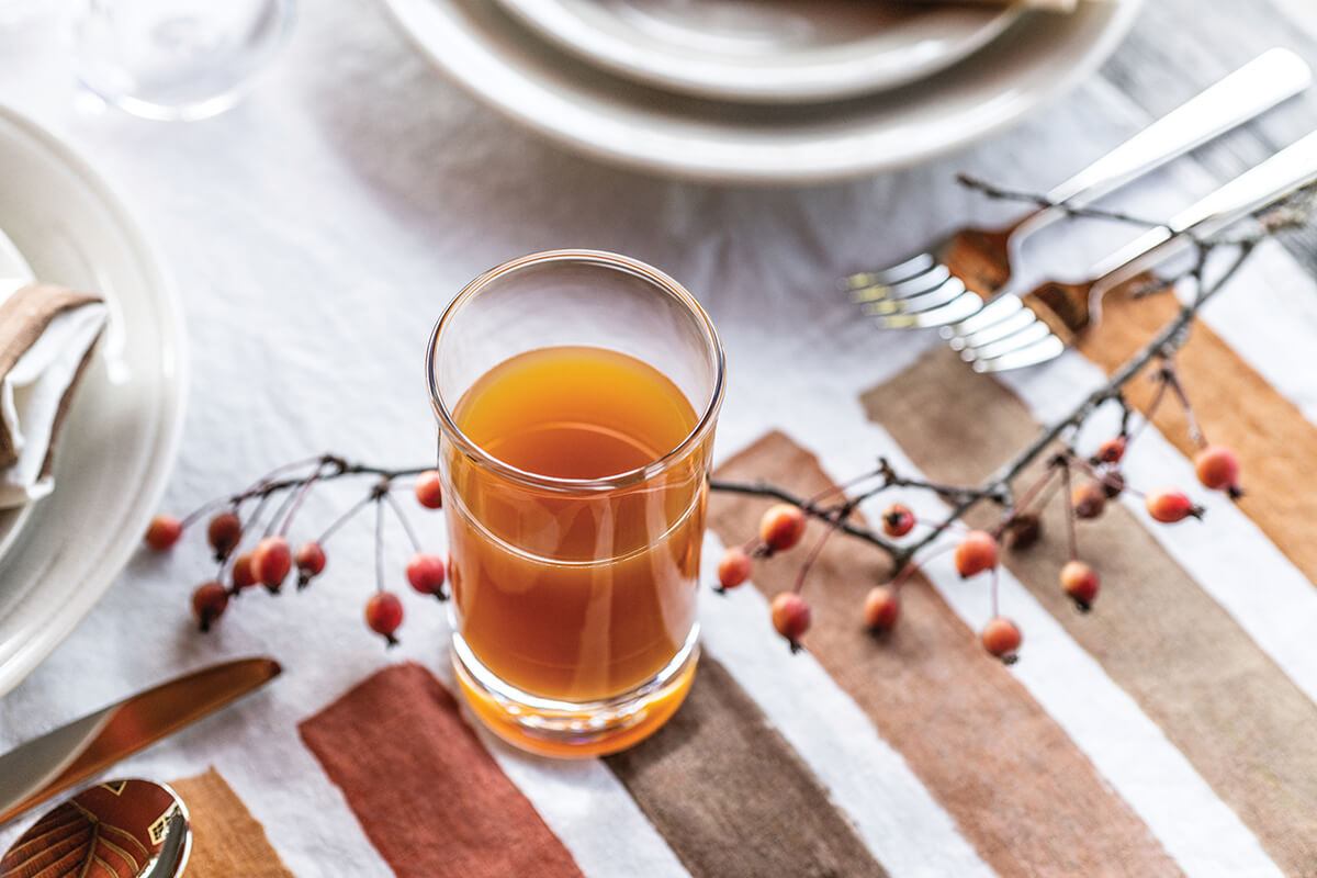 Two clear highball glasses filled with amber liquid on a striped table setting with plates and berries.