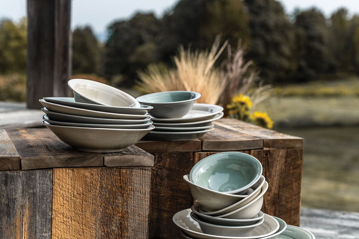 Stacked ivory and gray ceramic bowls and plates arranged on wooden blocks outdoors.