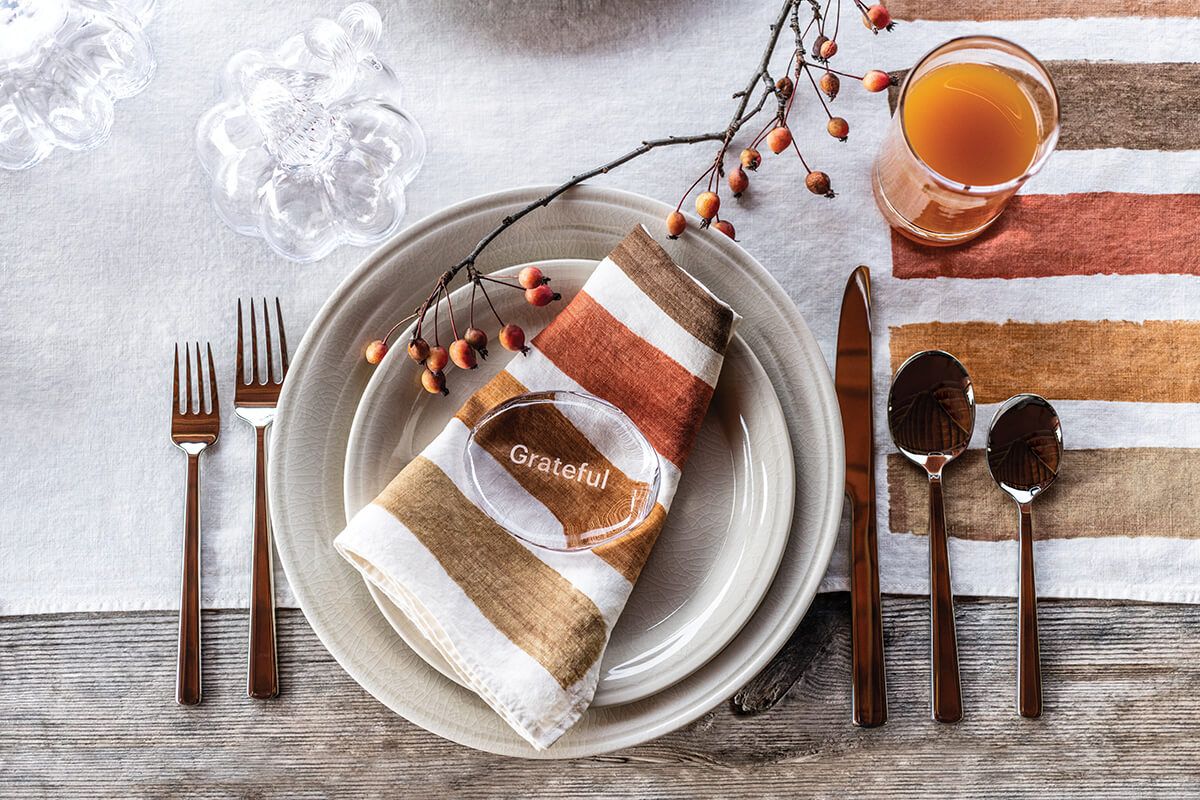 Ivory crackle dinnerware place setting with stacked plates, bronze flatware, and striped napkin.