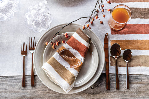 Round stone with "Grateful" text resting on striped napkin in place setting with autumn berries and flatware.