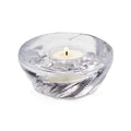 Clear glass shell-shaped tealight holder with lit white candle inside.