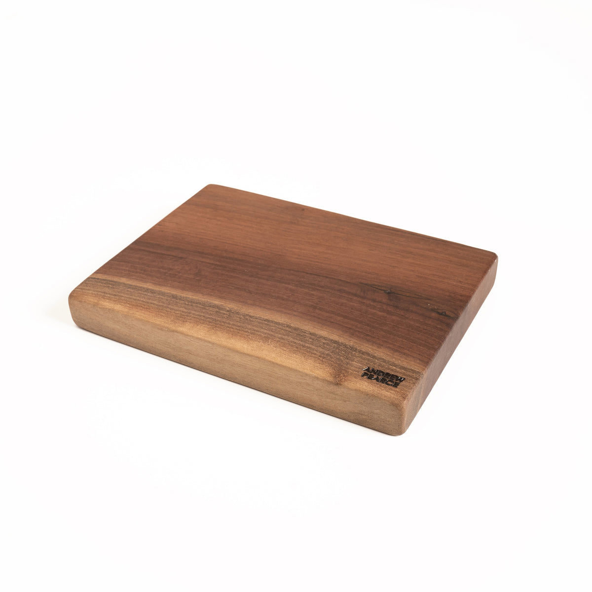Walnut cutting board with square edges and rounded corners, showing wood grain variation and maker's mark on lower edge.