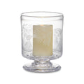 Clear glass hurricane with engraved pine branch design and cream-colored pillar candle inside.