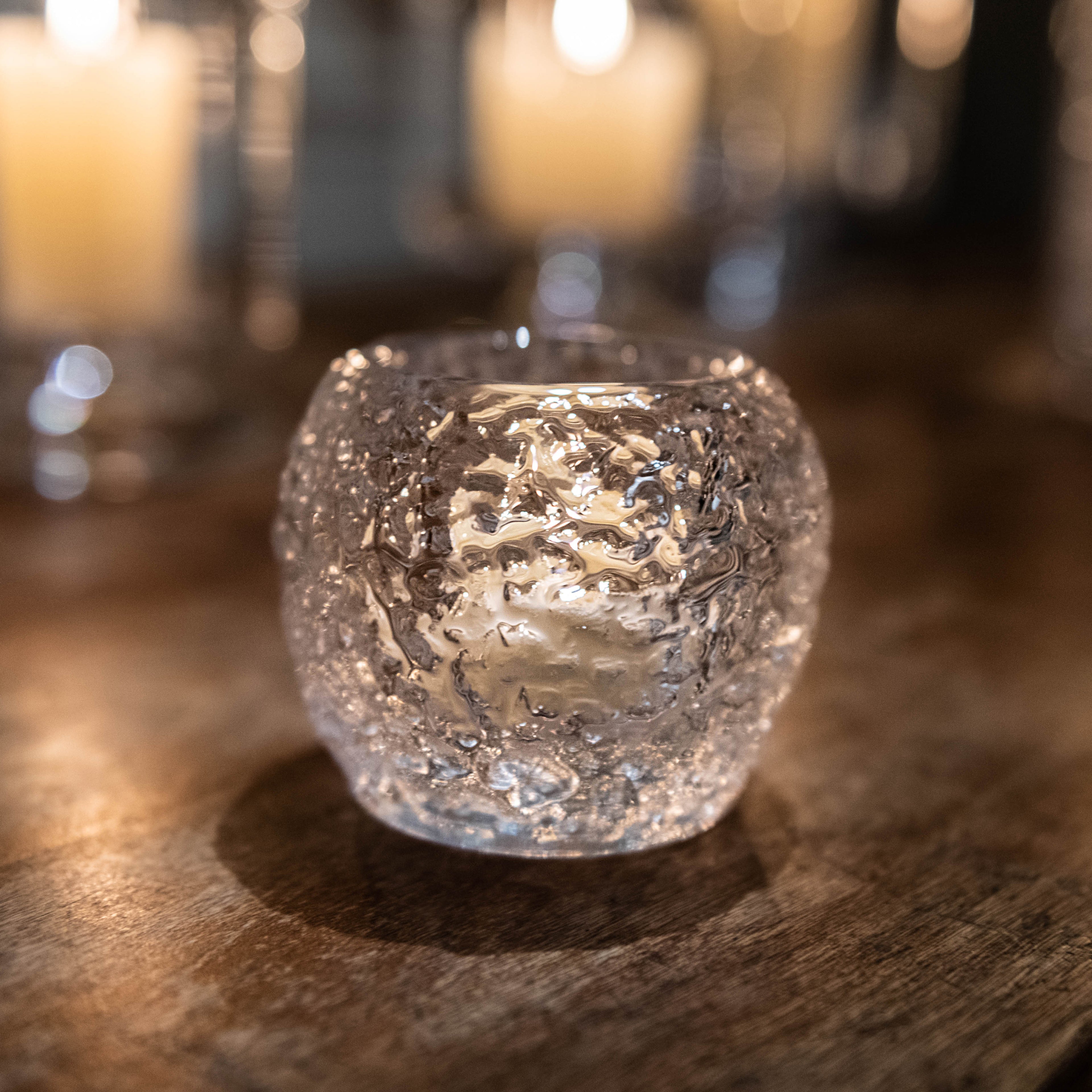 Lit tealight candle in a textured clear glass holder with warm glow.