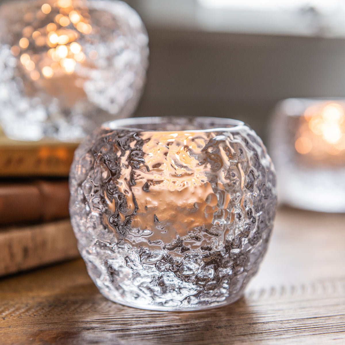 Three textured glass tealight holders with lit candles, featuring white crackle finish and warm glow.