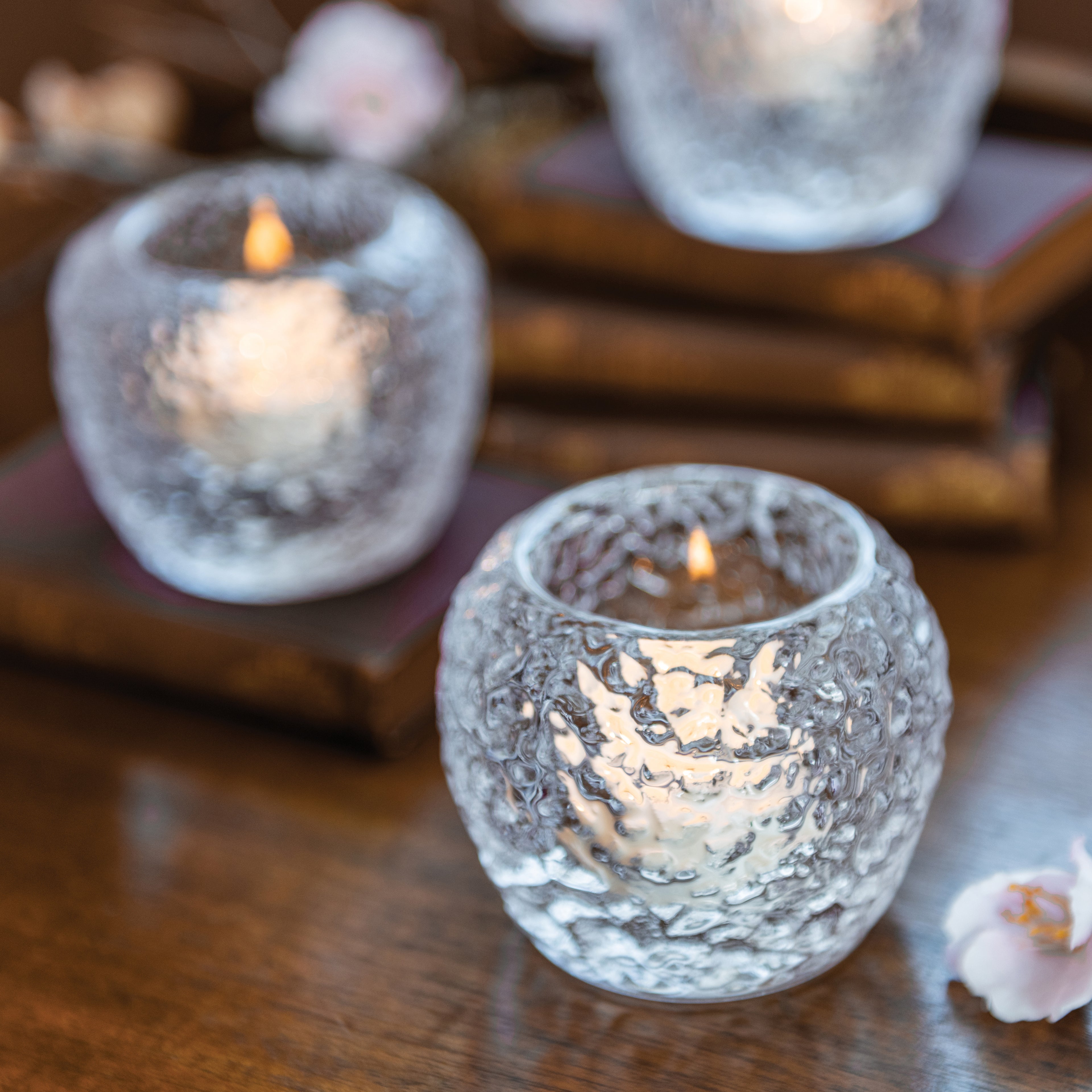 Three textured glass tealight holders with lit candles on a wooden surface.