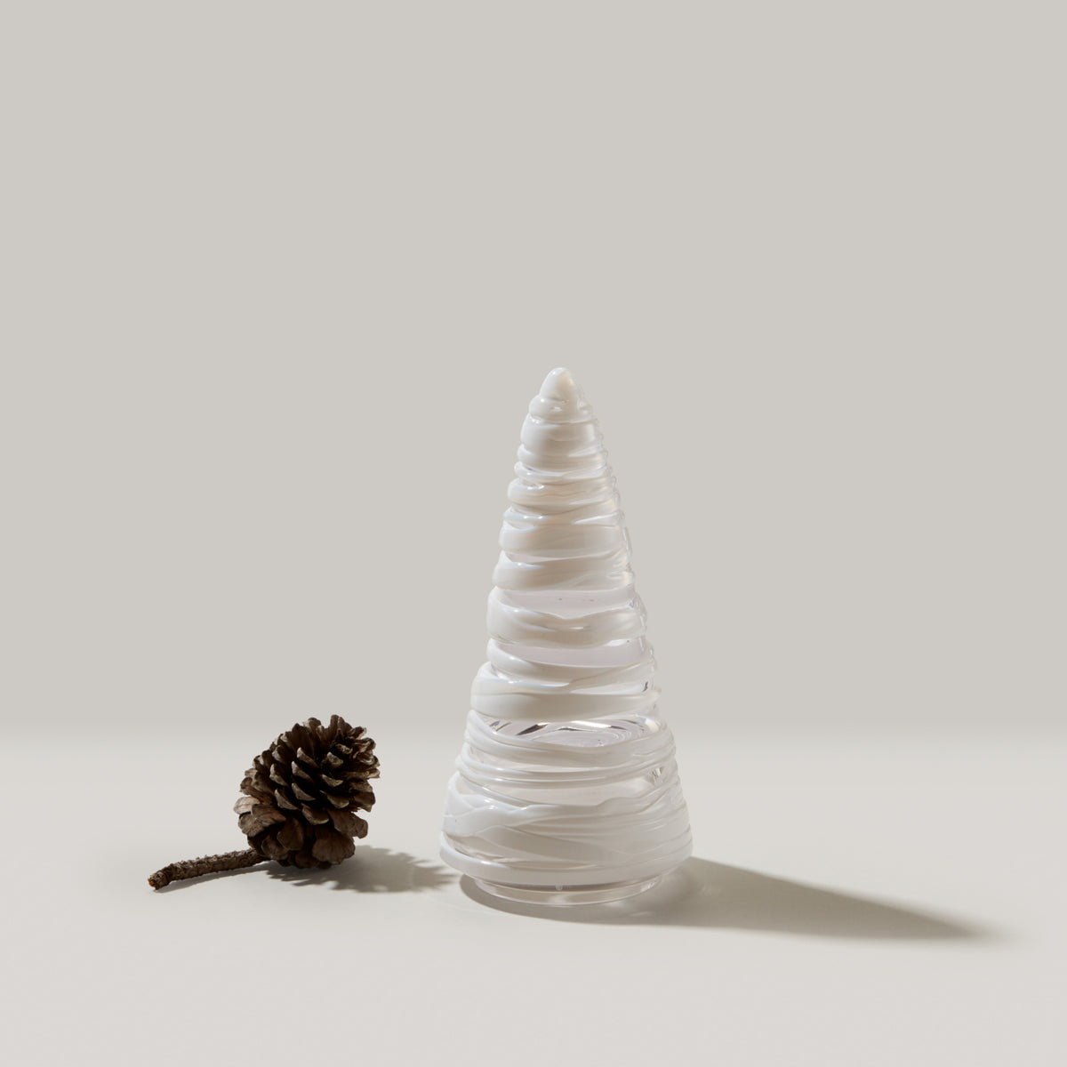White conical tree with layered bands and pointed top, displayed next to a brown pinecone.