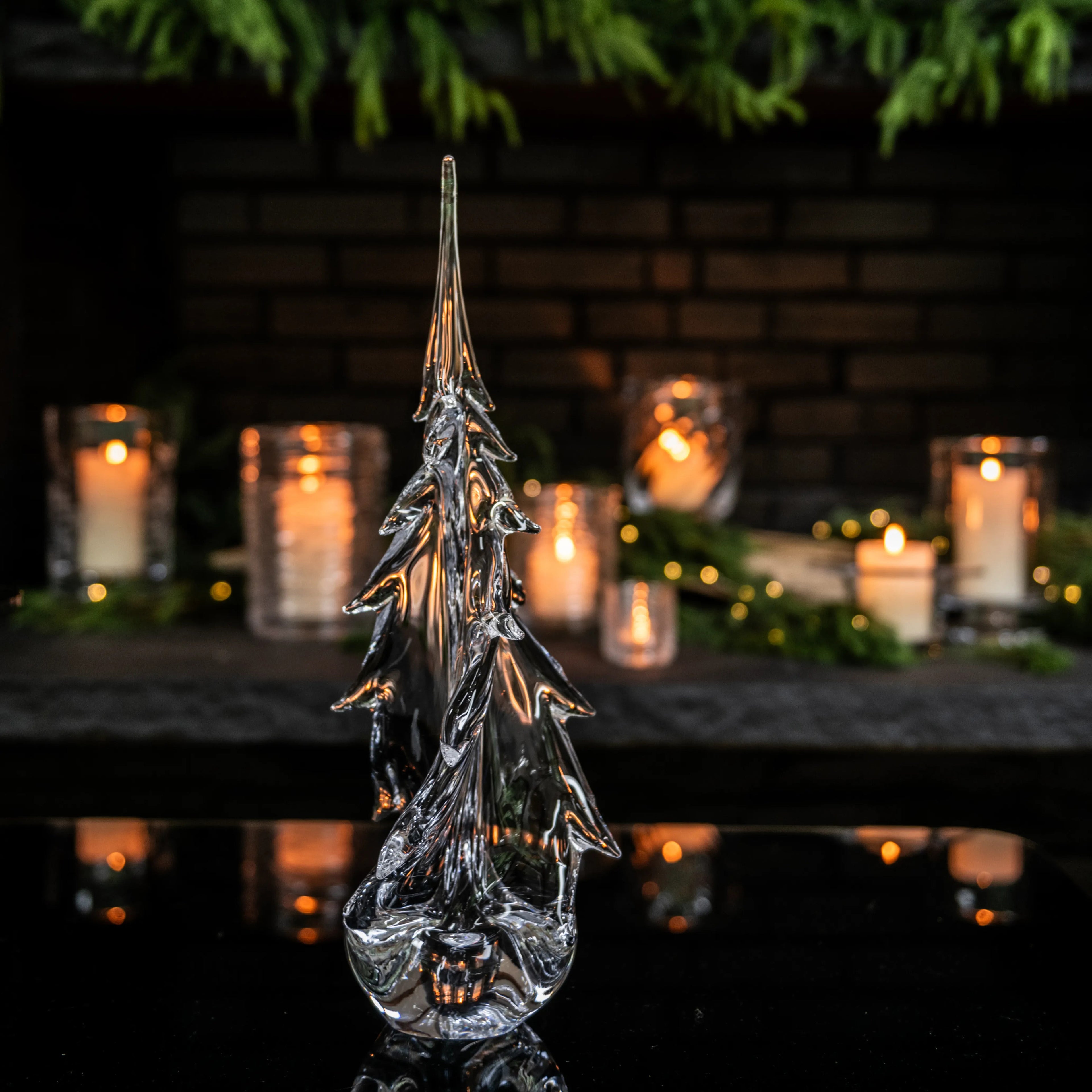 Clear glass evergreen tree sculpture with twisted branches and pointed top, displayed with candles in background.