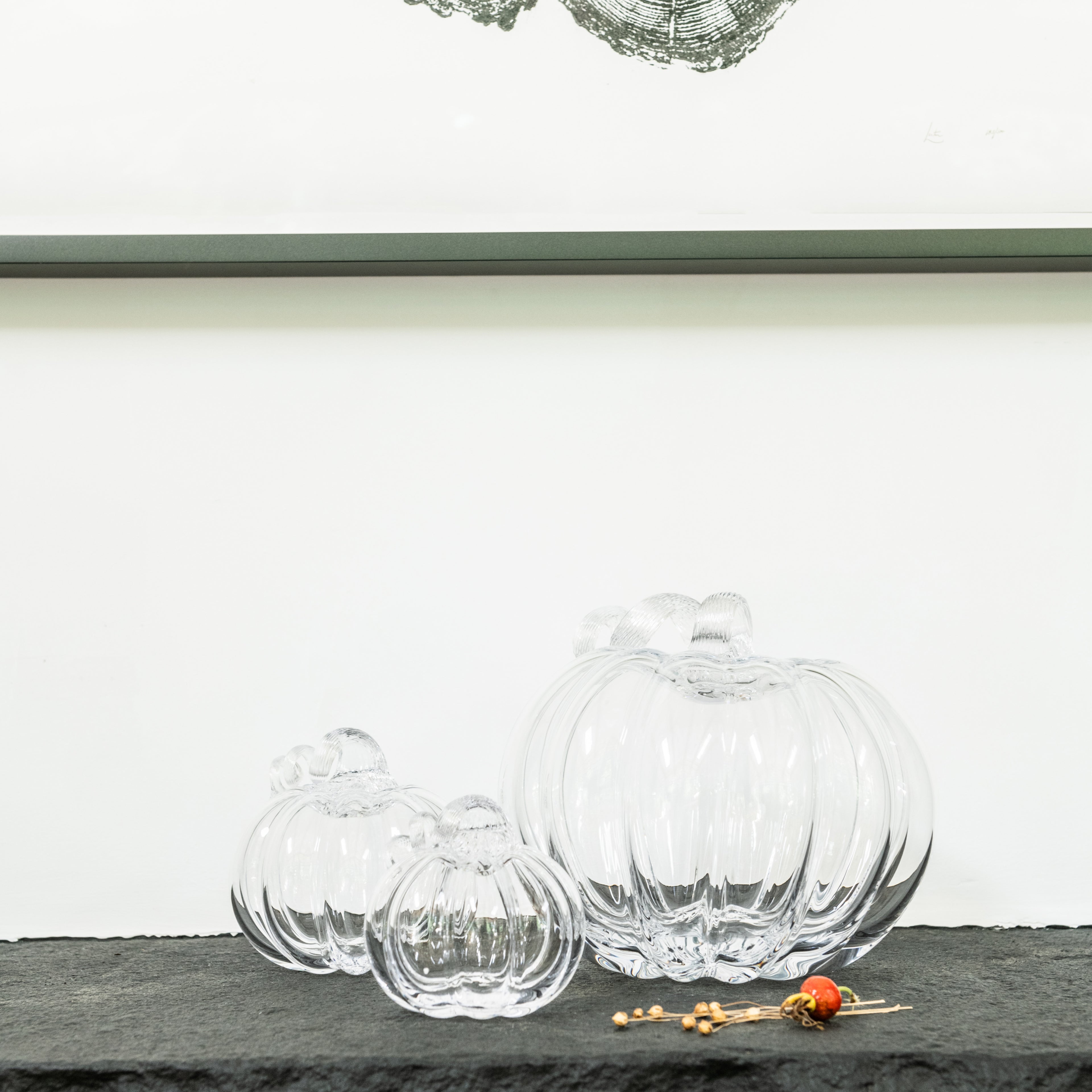 Three clear glass pumpkin-shaped objects in varying sizes with small golden beads beside them.