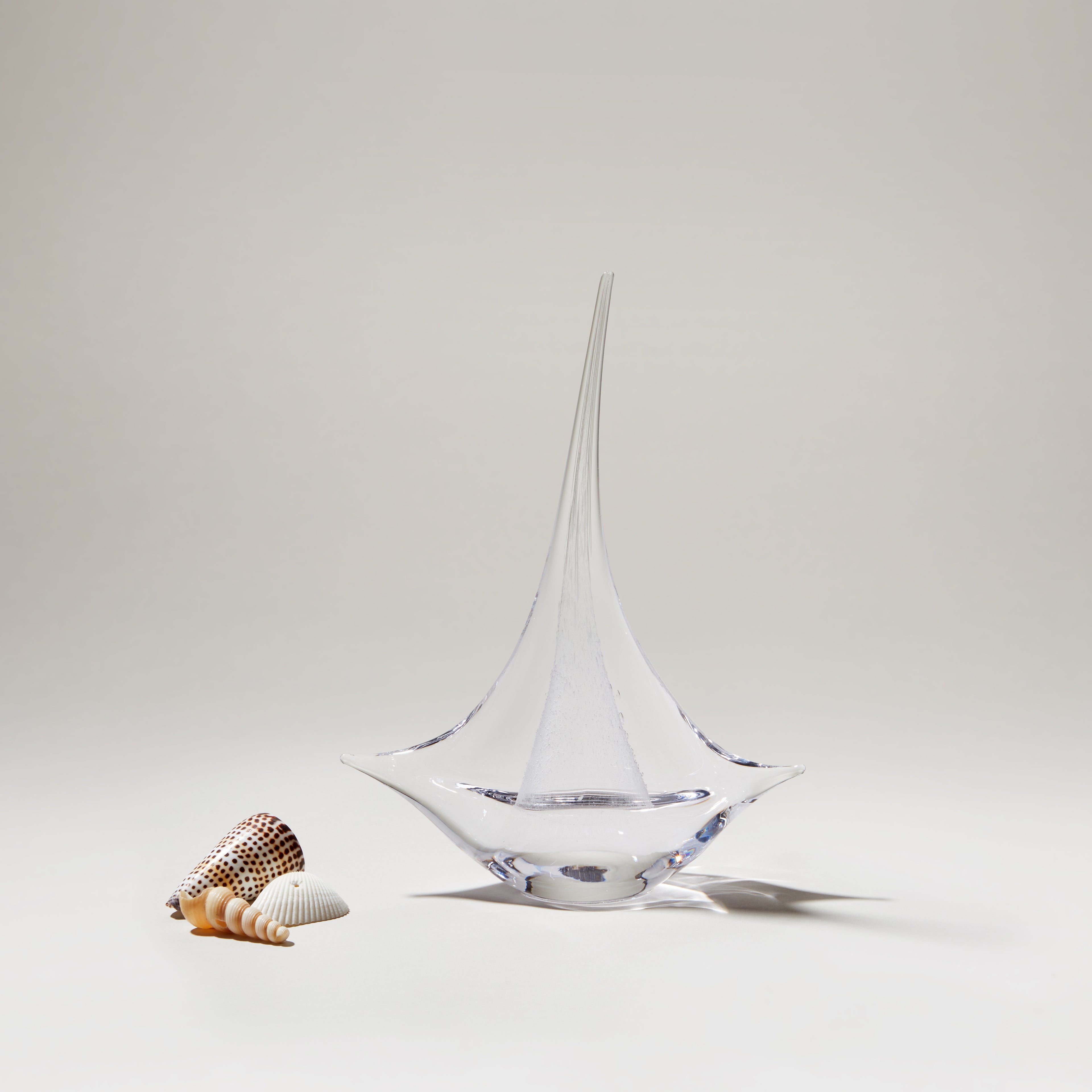 Clear glass sailboat with pointed sail and rounded base, displayed with small decorative shells.
