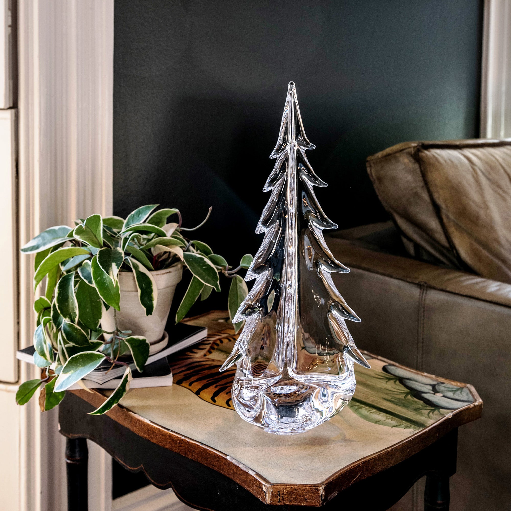 Clear glass evergreen tree figurine displayed on wooden table with potted plant.