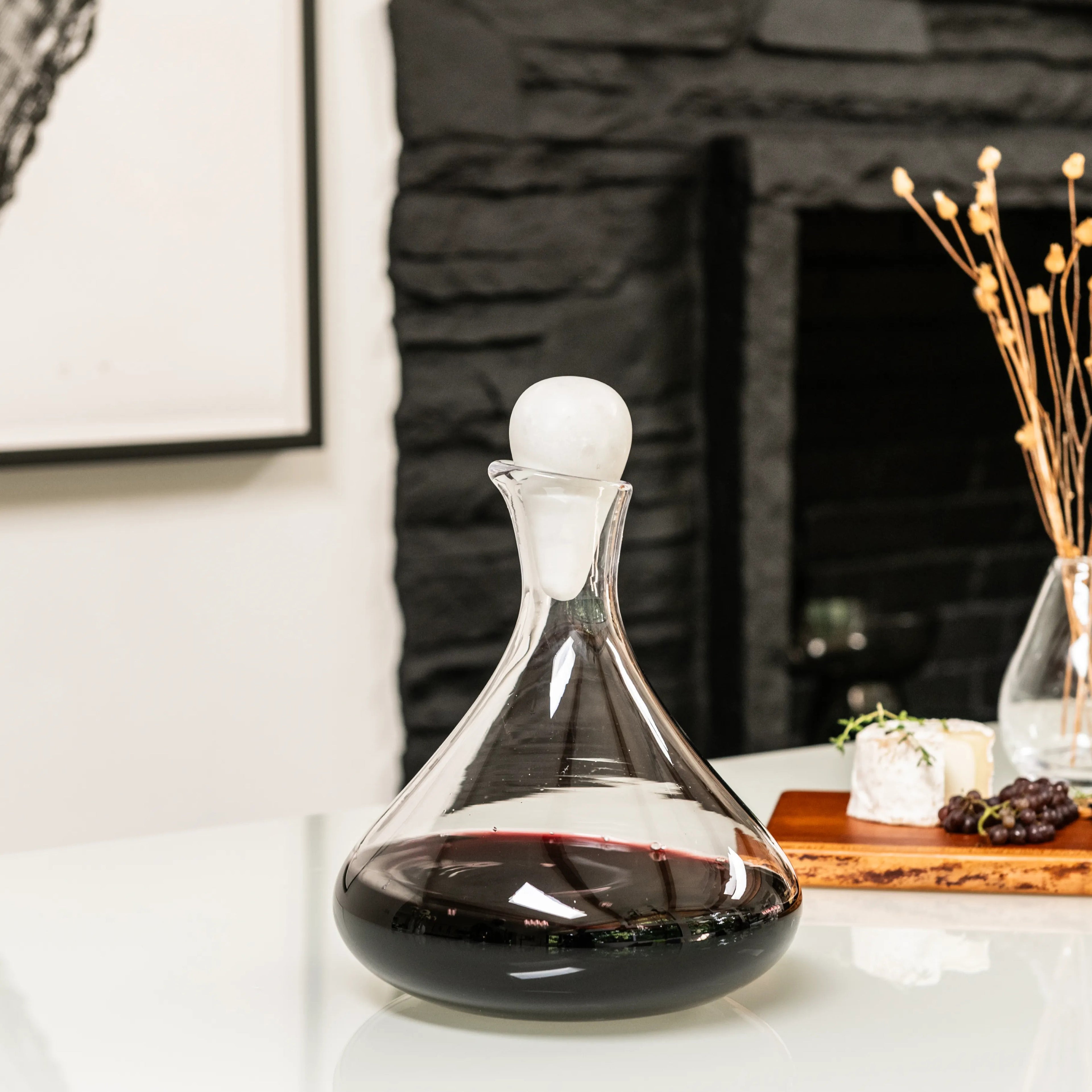 Clear glass wine decanter filled with red wine, topped with a white marble spherical stopper.