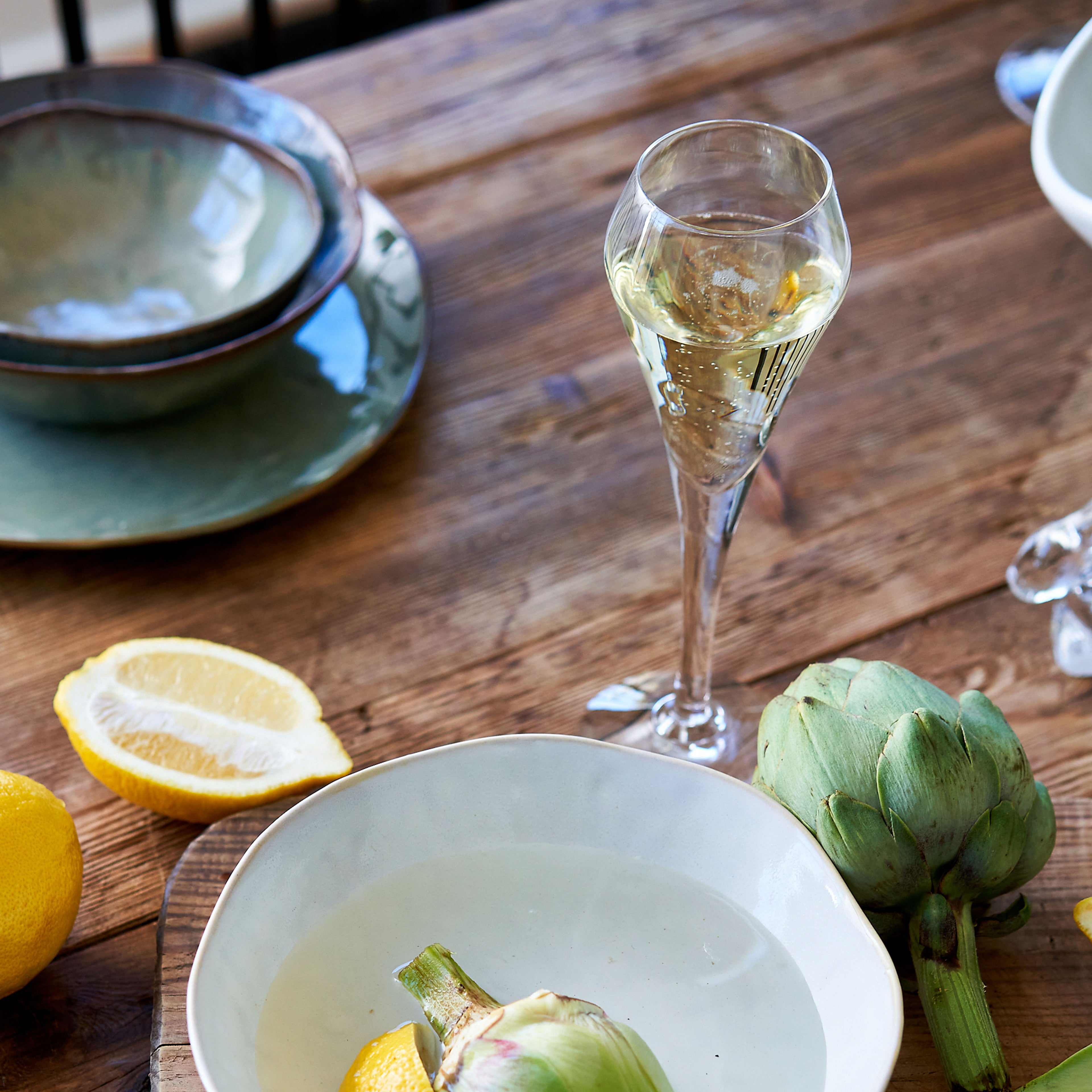 Two tall champagne flutes with clear glass stems, one filled with sparkling wine, on a wooden table.