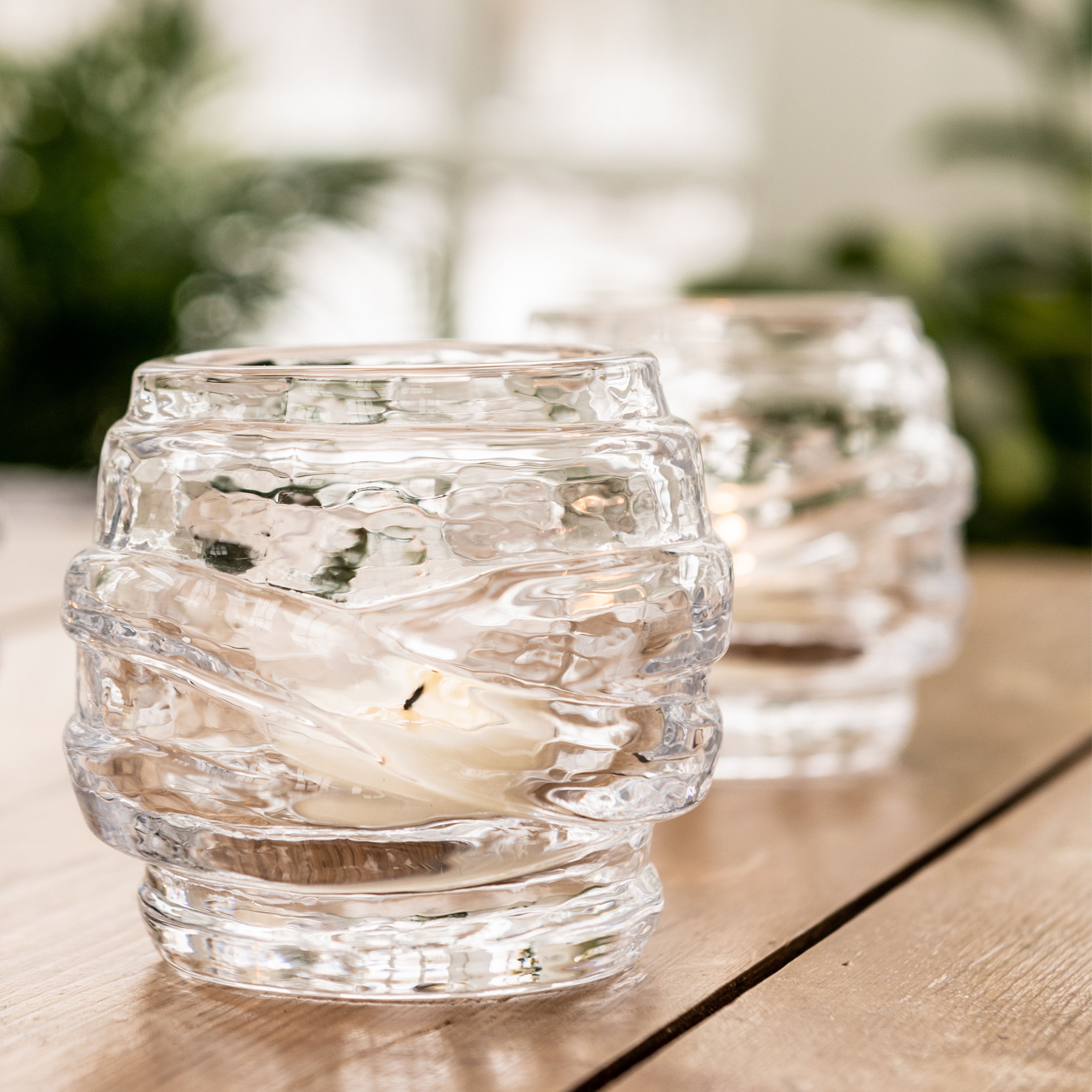 Two clear textured glass tealight holders with lit candles on wooden surface.