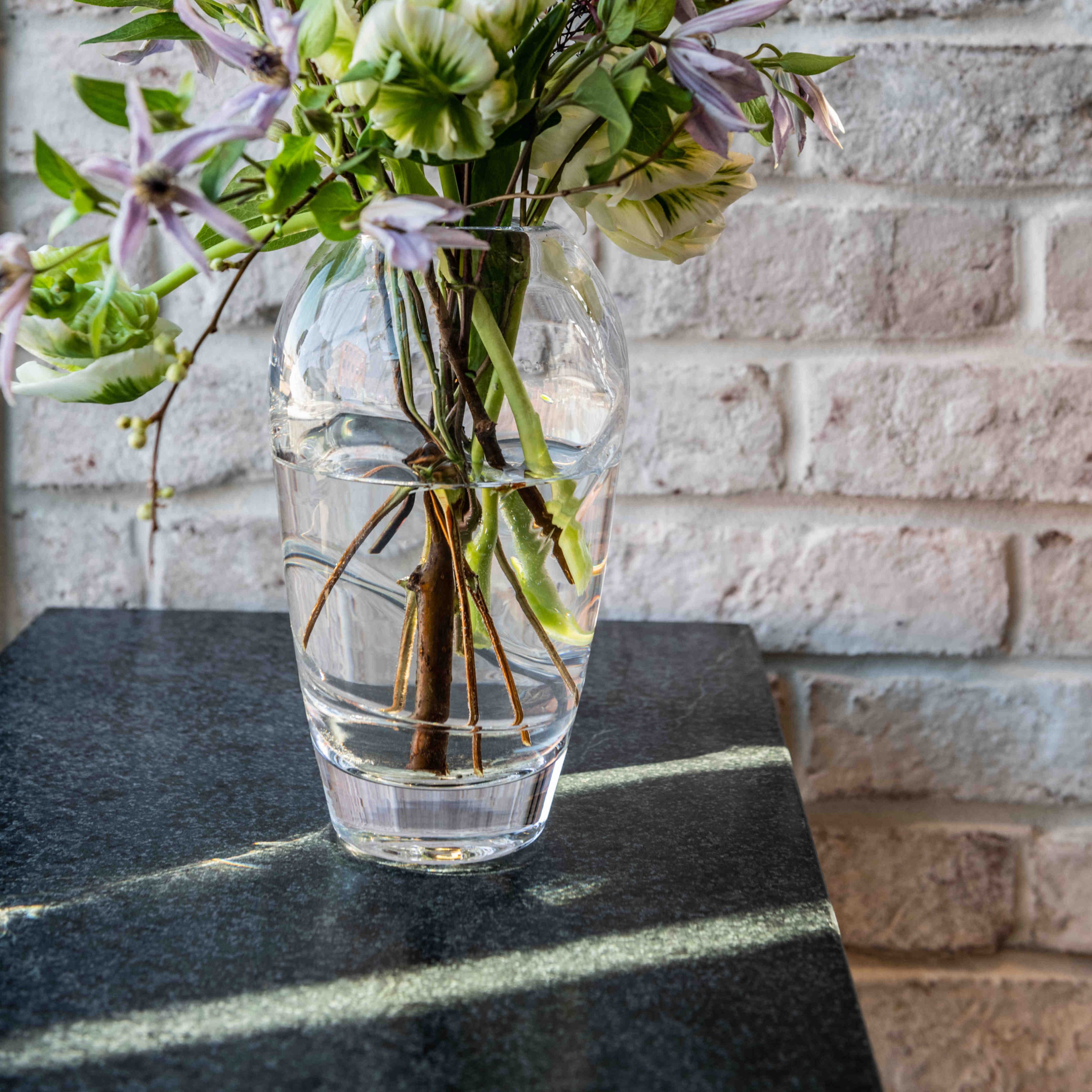 Clear glass vase with horizontal ribbed bands holding mixed green and purple flowers and foliage.
