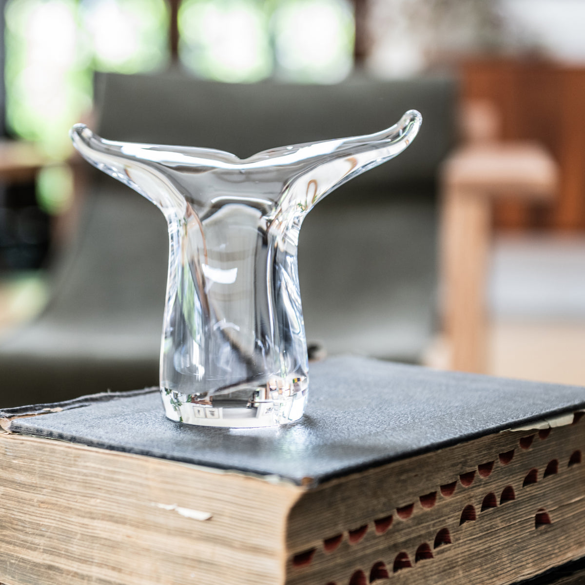 Clear glass whale tail-shaped sculpture sitting on an open book with dark pages.