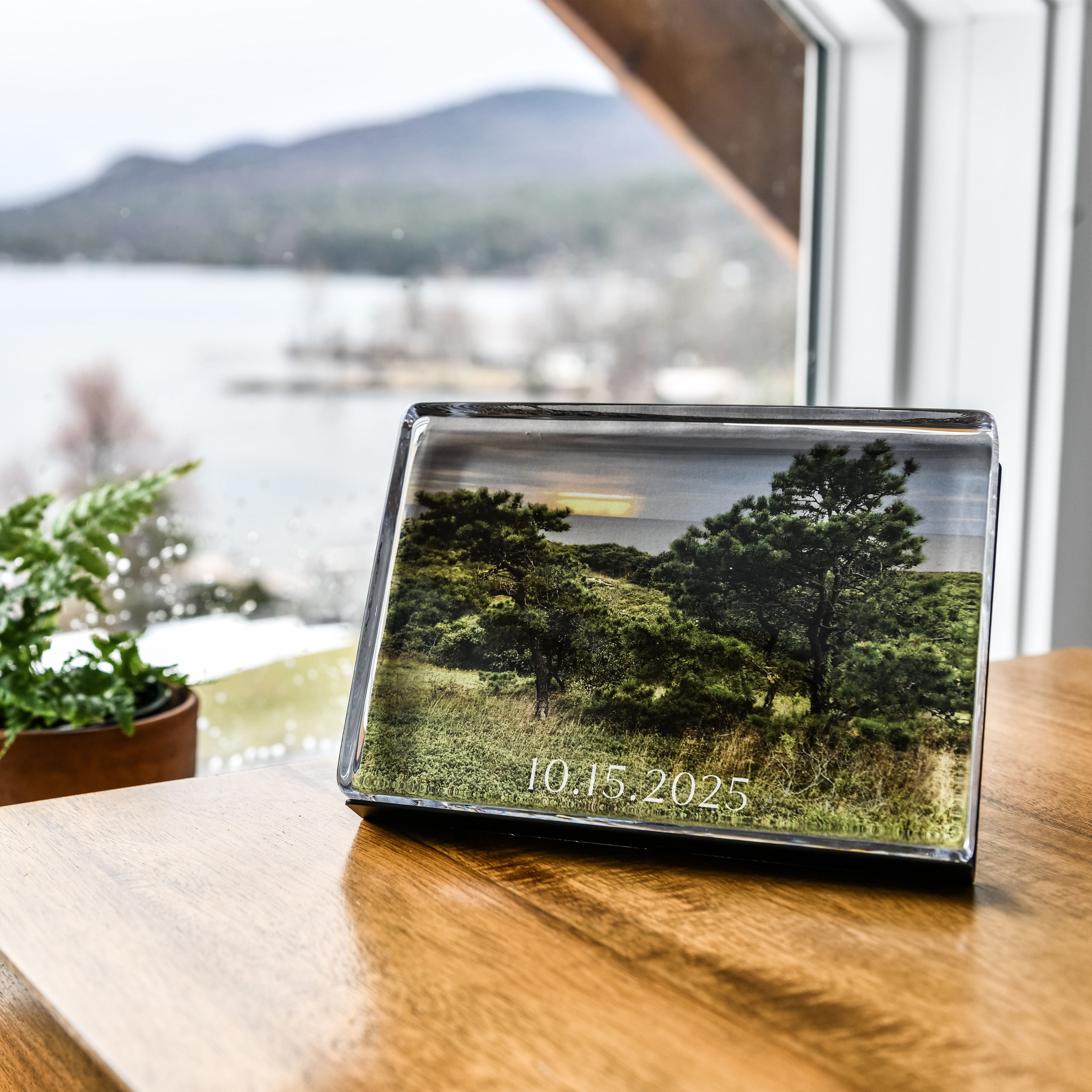 Clear acrylic photo block displaying landscape image with trees and date printed on surface, positioned on wooden table.