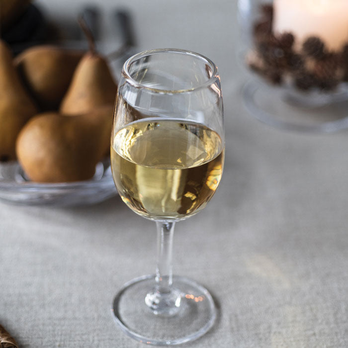 Glass of pale yellow wine with pears and decorative items blurred in background.