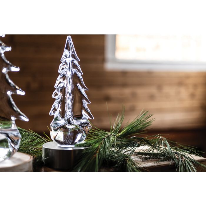 Clear glass tree figurine with textured surface on black base, surrounded by fresh evergreen branches.