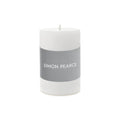White cylindrical pillar candle with gray band labeled "SIMON PEARCE" and visible wick on top.