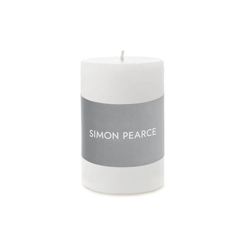 White cylindrical pillar candle with gray band labeled "SIMON PEARCE" and visible wick on top.